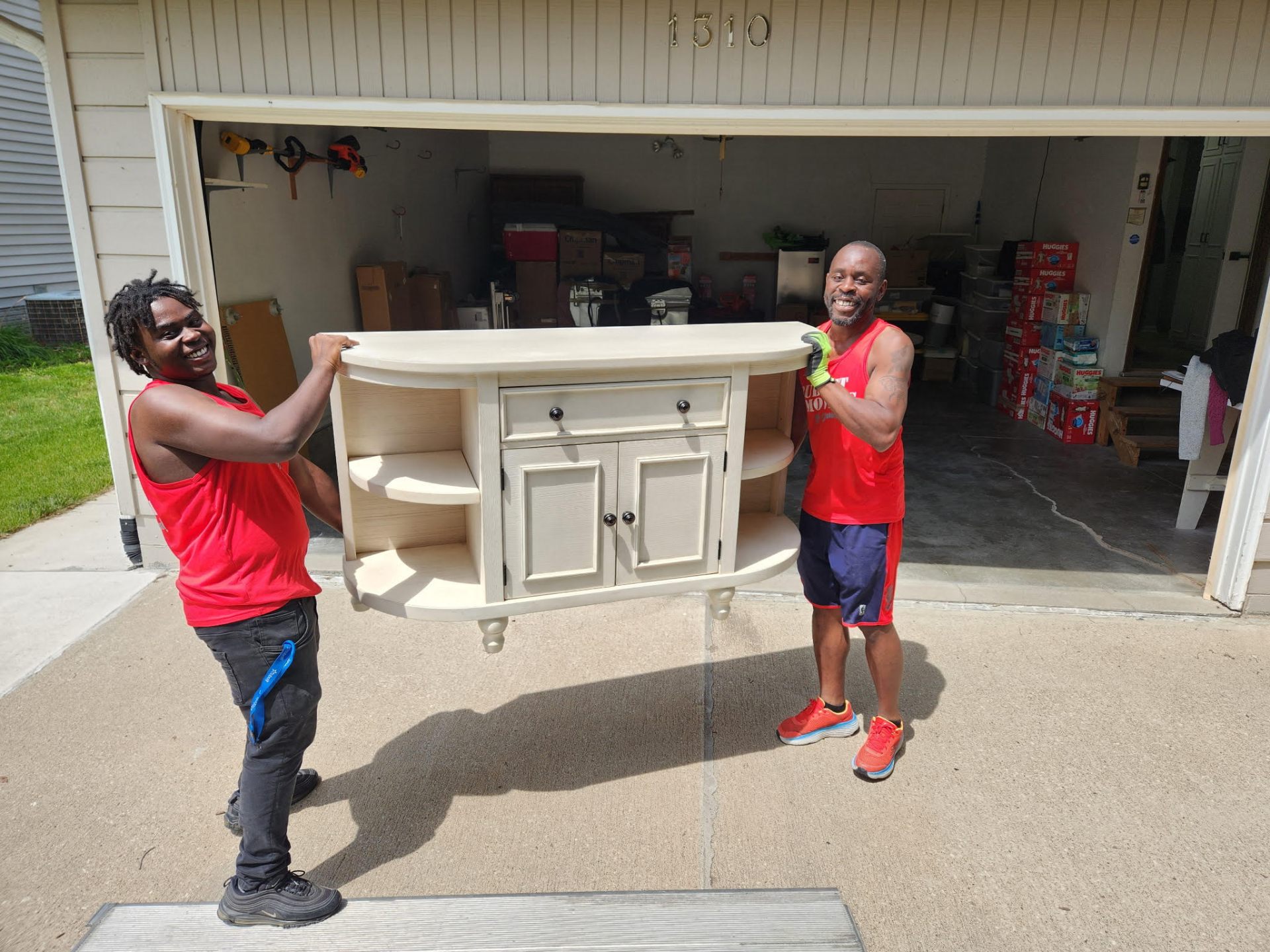 Two Budget Movers carrying a cream-colored sideboard out of a garage