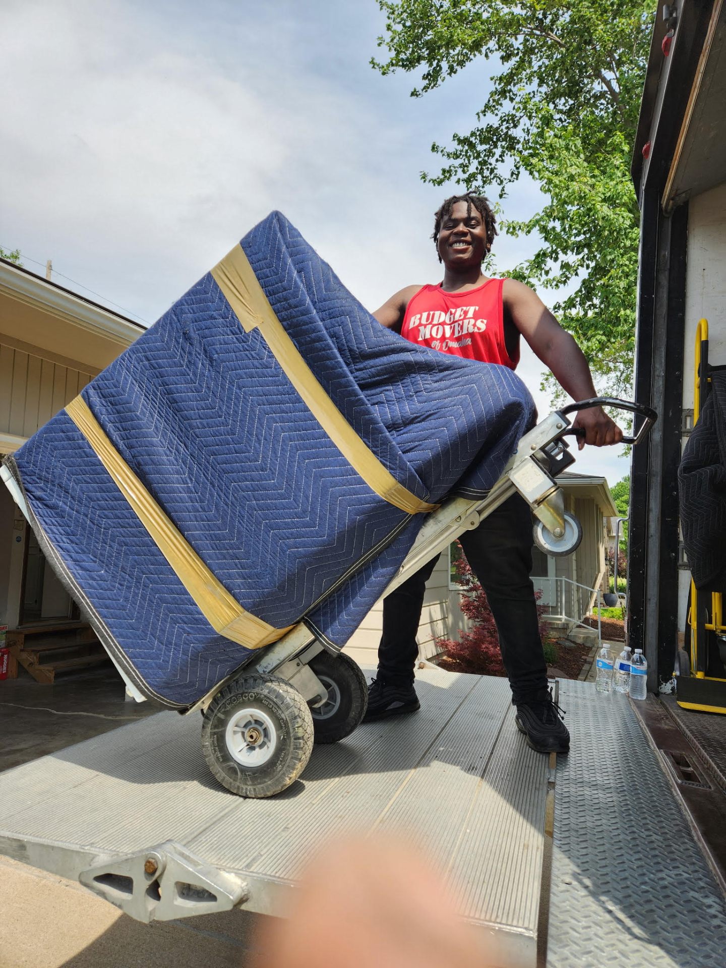 Budget Movers team member moving a wrapped mattress on a dolly
